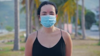 Coronavirus salgınından kalma maske takan genç bir kadının portresi sokakta koruyucu bir talep taşıyor. Kadın siyah elbisesinin önünde dikiliyor, uzaklara bakıyor. Sağlık ve güvenlik hayatı kavramını, Covid-19 'u, salgını kelime olarak kabul et..