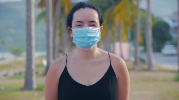 Retrato de mujer joven en una máscara de una epidemia de coronavirus lleva demanda protectora en la calle. La mujer está de pie vestido negro mirando hacia otro lado. Concepto de salud y seguridad de la vida, Covid-19, pandemia de palabra . — Vídeos de Stock