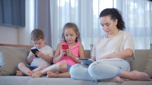 Familia feliz, mamá y niños pequeños y lindos ven el teléfono, mamá juega con los niños en casa, relajarse con un teléfono inteligente, abrazos, sentarse en el sofá, reír, divertirse, disfrutar de momentos de la vida familiar — Vídeos de Stock