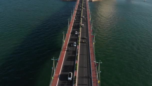 Tiro Vuelo aéreo no tripulado desde la vista superior del puente de la ciudad con coches y motos contra el telón de fondo del hermoso mar del océano y los grandes edificios de la ciudad. Puente y autopista de ciudad. — Vídeo de stock