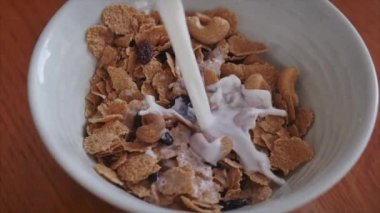 Kahvaltı konsepti, sağlıklı bir diyet, fındıklı tahıl gevreği ve ahududu dilimleri ve kuru üzüm. Müsli kahvaltı gevreğinin içine yavaş yavaş süt dökülüyor. Sağlıklı yemek.