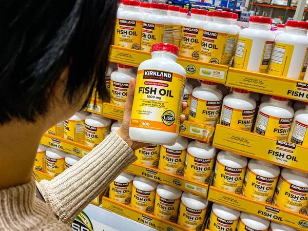 Kirkland İmza Balık yağı taşıyan kadın Costco depo koridorunda 1000mg..