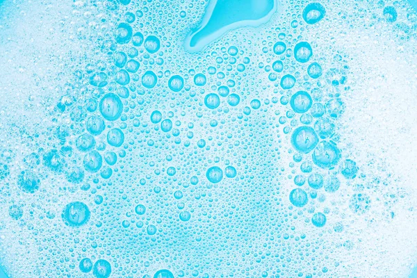 Close-up White Foam with bubbles on surface of water, washing powder with soap and blue bath, abstract background transparent bubble.