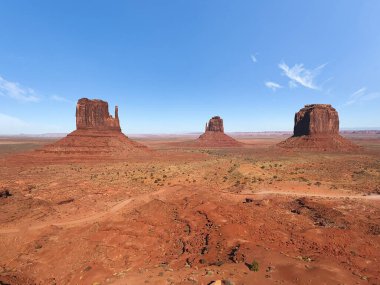 Kırmızı çöl, mavi gökyüzü ve sabahları bulutlarla anıt vadisinin muhteşem manzarası. Arizona 'da West Mitten Butte, East Mitten Butte ve Merrick Butte ile anıt vadisi. 