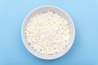 Mavi arka planda beyaz kasede taze süzme peynir. Süt kaymağı tabakta. Üst görünüm. 