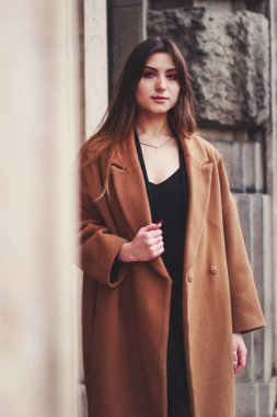 Siyah elbiseli ve uzun kahverengi ceketli bir manken. Siper. Tarz. Moda.