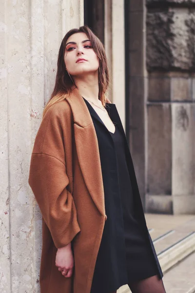 Model in zwarte jurk en lange bruine jas. Een moersleutel. Stijl. Mode — Stockfoto