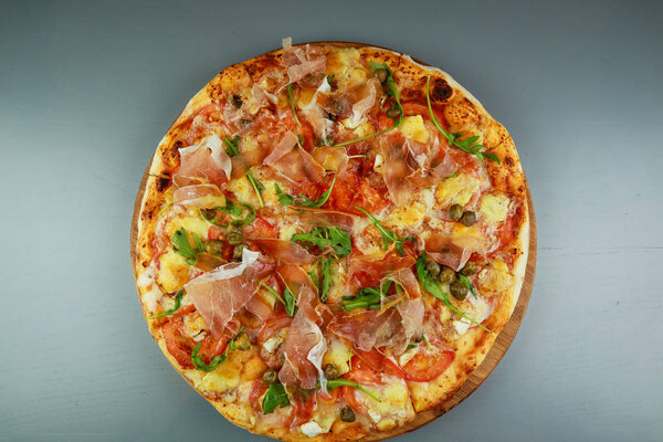 The pizza is prosciutto. Capers, tomatoes, arugula, mozzarella, 