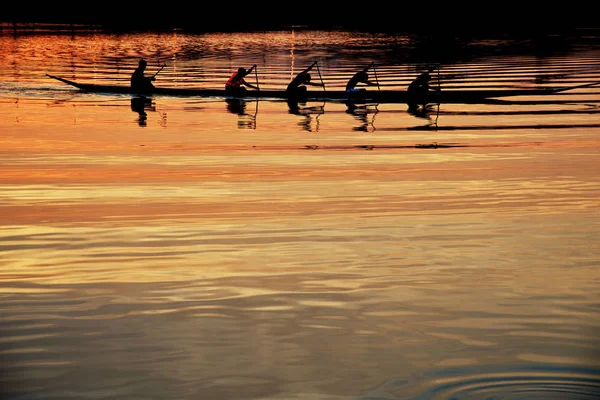 Teamarbeit junger Männer in einem Ruderboot bei Sonnenuntergang — Stockfoto