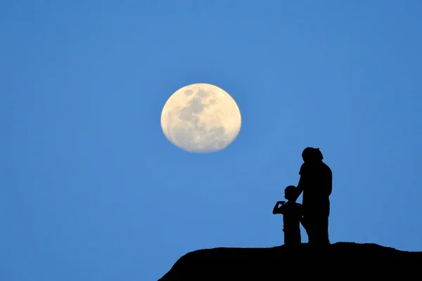 Silhueta de mãe e filho em pé na montanha, observando o fundo azul da lua . — Fotografia de Stock