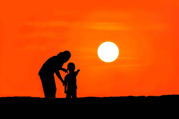 La silhouette de la mère et du fils debout sur la montagne regardant le coucher du soleil . — Photo