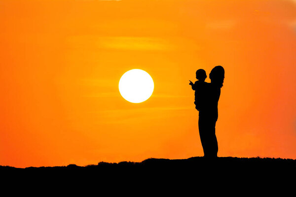 Black silhouette of a mother carrying her son watching the sunset on mountain orange background