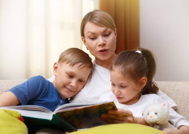 Güzel anne genç çocuklarına bir kitap okuyor. Kız ve erkek kardeş bir hikaye için dinleme.