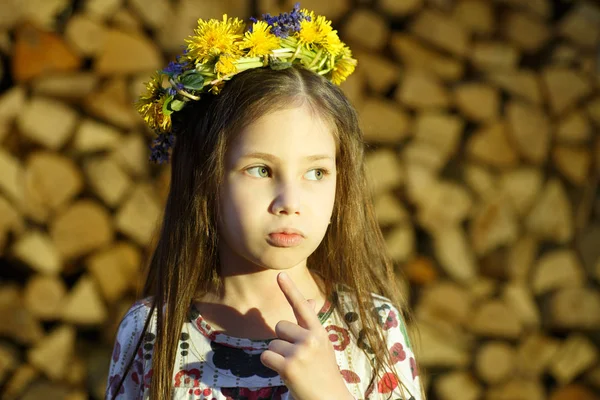 Joven chica bonita en flores corona se queda cerca de la pila de madera en el pueblo . — Foto de Stock