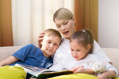 Güzel anne genç çocuklarına bir kitap okuyor. Kız ve erkek kardeş bir hikaye için dinleme.