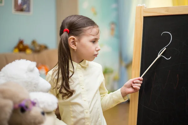 Pequena professora. Menina bonita está ensinando brinquedos em casa em Imagens Royalty-Free