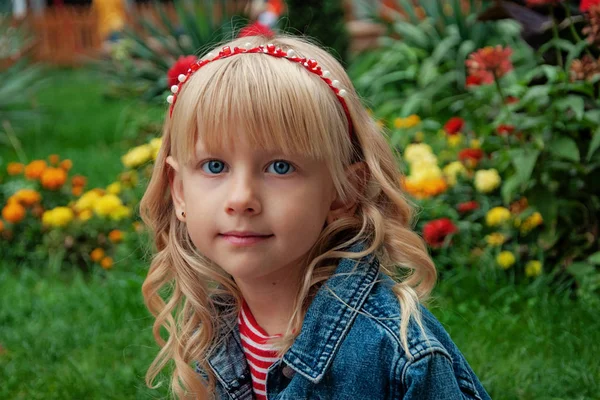 Χαριτωμένο κοριτσάκι με σγουρά ξανθά μαλλιά σε ένα πάρκο μια καλοκαιρινή μέρα — Φωτογραφία Αρχείου