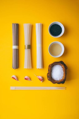 Düz stil, Asya pirinç noodle, soba ve udon siyah susam ve pirinç sirke, tuz bir ahşap kase, karanfil sarımsak ve chopsticks sarı bir arka plan üzerinde bir kase ile. Minimalizm
