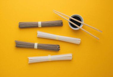 Asya Erişte udon ve soba, yemek çubukları, susam bir kase parlak sarı zemin üzerine siyah. Minimalizm. Düz yatıyordu. 