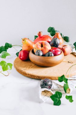Assorted fruits in a wooden plate on a marble background, green ivy mango, peach, plum, pear, pomegranate, fig peach