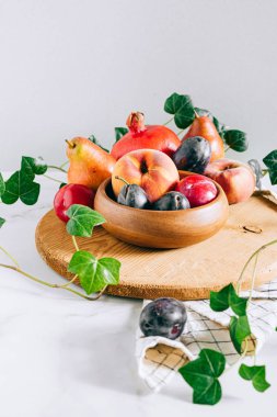 Assorted fruits in a wooden plate on a marble background, green ivy mango, peach, plum, pear, pomegranate, fig peach