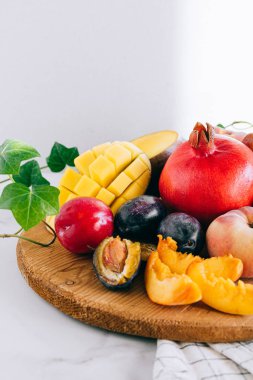 Assorted fruits in a wooden board on a marble background, green ivy mango, peach, plum, pear, pomegranate, fig peach