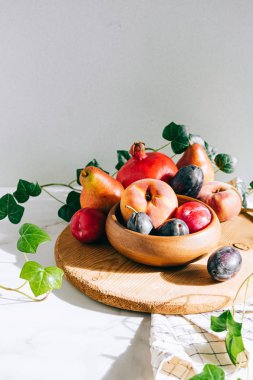 Assorted fruits in a wooden plate on a marble background, green ivy mango, peach, plum, pear, pomegranate, fig peach