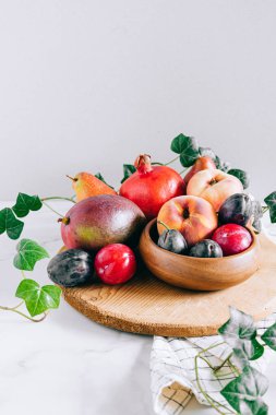 Assorted fruits in a wooden plate on a marble background, green ivy mango, peach, plum, pear, pomegranate, fig peach
