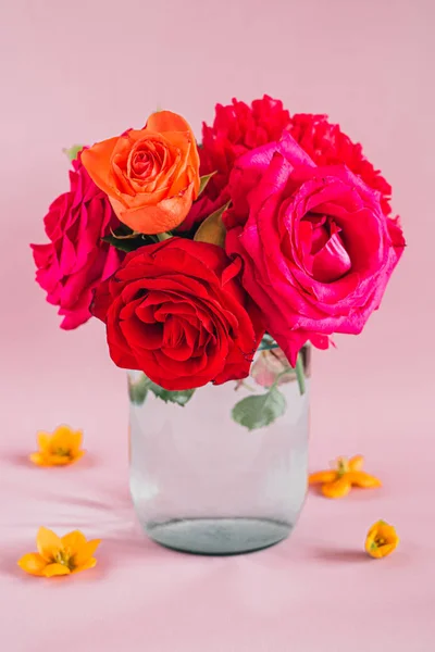 Bouquet of red and pink peonies and roses in a glass vase with water on a pink background