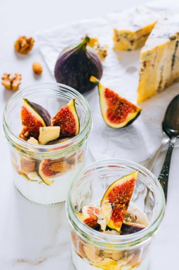 Ekşi krema, vanilya, incir, fındık, bal ve mavi peynir bir bardak mermer arka planda