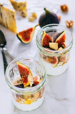 Ekşi krema, vanilya, incir, fındık, bal ve mavi peynir bir bardak mermer arka planda