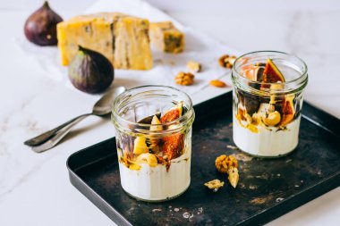 Ekşi krema, vanilya, incir, fındık, bal ve mavi peynir siyah bir tepside, mermer arka planda