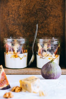 Ekşi krema, vanilya, incir, fındık, bal ve mavi peynir, ahşap bir kutuda, mermer arka planda.