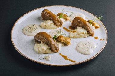 Domuz mantarlı kuskus garnitürlü kuzu dilleri ve siyah arka planda taze bezelye filizleri.