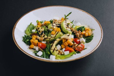 Balkabaklı sıcak salata, ızgara avokado, vişneli domates ve siyah arka planda beyaz peynir.