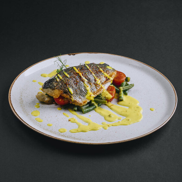 Dorado fillet with green beans, cherry tomato and curry sauce on a black background