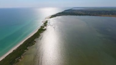 A picturesque bird`s eye view of the Black Sea sandy spit covered with wetland forming a round inlet and dividing sea waters in dark green and bright blue on a sunny day in summer.