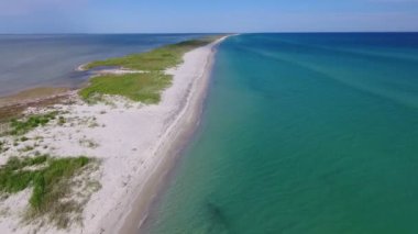 A bird`s eye view of the straight Black Sea sandy stripe with dark wetland separating sea waves in violet and bright blue on a sunny day in summer. The narrow spit looks emigmatic and fine