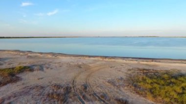 A bird`s eye view of the Black Sea sandy coast with areas of green and brown grass and bright blue waters on a sunny day in summer. The shelf is shot from a low flying drone. It looks mysterious