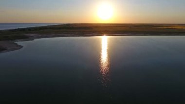 A beautiful bird`s eye view of the Black Sea sandy spit with dark rusty wetland at golden sunset in summer. The sparkling sun path looks gorgeous on calm sea waters in picturesque twilights.