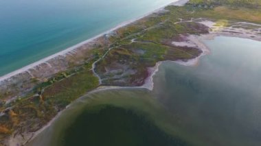 A breathtaking bird`s eye view of the Black Sea sandy spit, covered with green grass and twisting pathways, small bay and shining waters full of seaweed and alga at sunset in summer.