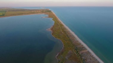 A gorgeous bird`s eye view of the Black Sea sandy spits in a triangular shape, covered with green grass and pathways, small bay and shining waters full of seaweed at splendid sunset in summer.