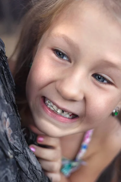 Una niña pequeña cerca de un pino muestra un diente de bebé tambaleante en su —  Fotos de Stock