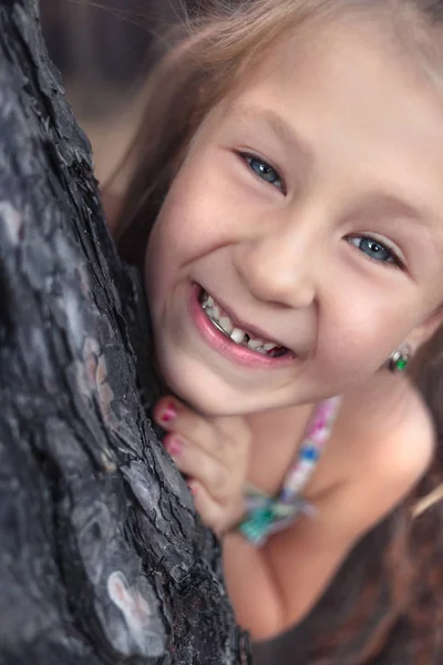 Uma menina perto de um pinheiro mostra um dente de leite oscilante em seu — Fotografia de Stock