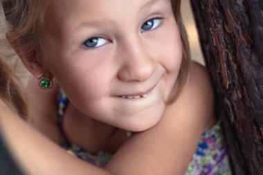 Çam ağacının yakınında küçük bir kız, ağzında sallanan bir bebek dişi gösterir.