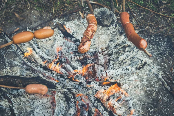 Cooking fried sausages on a fire in the forest. Toned, style photo.