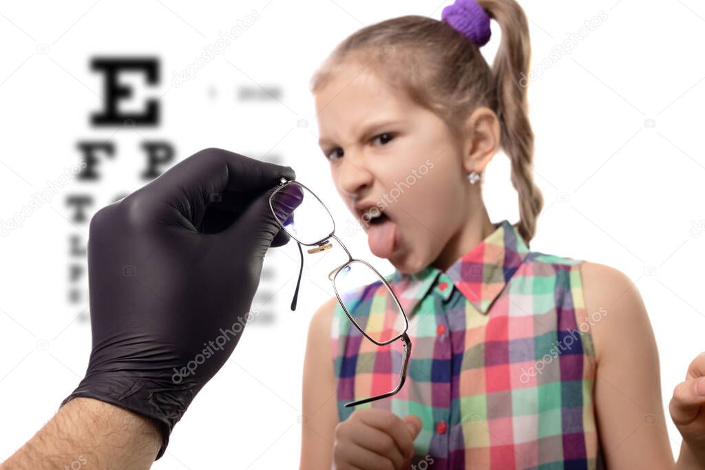Doctor ophthalmologist gives little cute girl her new glasses. The reaction of the child to wearing glasses. Studio photo on a white background.
