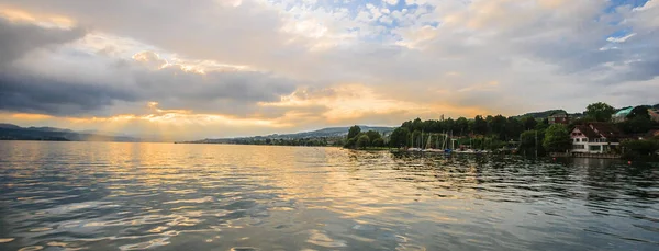 Panoramic summer view of boat cruise excursion landscape on Zurichsee with beautiful sunset shining light through clouds reflected the golden light on the water surface as a background.
