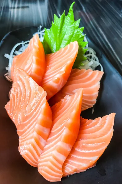 Japanese food: salmon sashimi (fresh raw salmon meat) decorated with grated turnip and mint leaf on wooden table as a background. — Stock Photo, Image