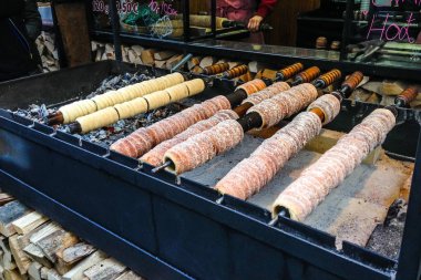 Trdelnik, traditional dessert baked in an open fire wooden stake in Prague Christmas Market, made from rolled dough that is wrapped around a stick, then grilled and topped with sugar and walnut mix clipart